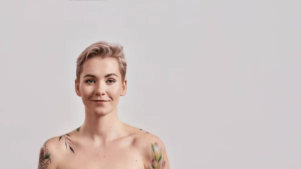 Retrato de una joven atractiva mujer semidesnuda tatuada con la piel perfecta sonriendo a la cámara aislada sobre un fondo claro — Foto de Stock