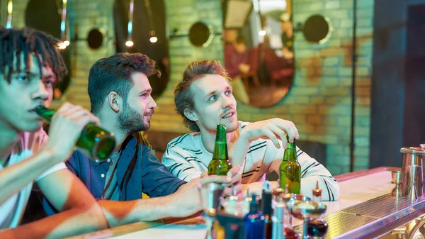 Noche de juegos. Tres jóvenes bebiendo cerveza mientras miraban el partido. Amigos pasando tiempo en el bar de deportes, entusiasmados con el juego — Foto de Stock