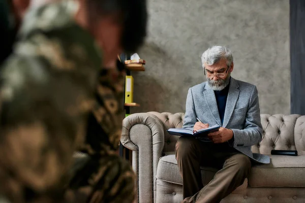 Proces van opstaan. Volwassen psycholoog communiceert met militairen en maakt notities tijdens therapiesessie. Soldaat lijdt aan depressie, psychologisch trauma. PTSS-concept — Stockfoto