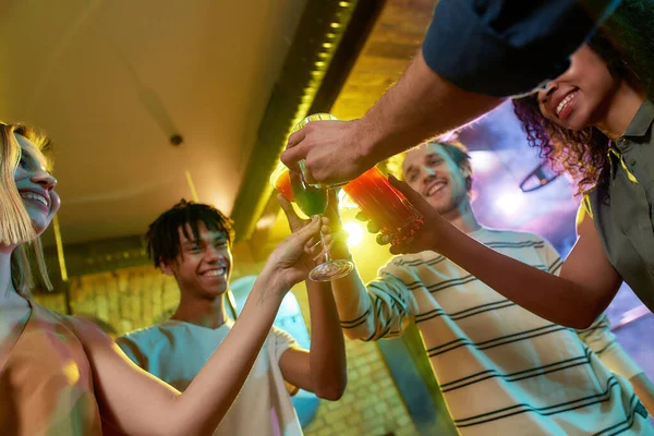 Där natten aldrig tar slut. En grupp vänner, unga kvinnor och män skålar medan de har roligt, dricker cocktails, umgås på nattklubben — Stockfoto
