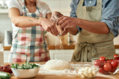 Çiftin hamuru hazırlarken kesilen görüntüsü. Önlüklü genç adam ve kadın evde pizza yapıyor. Hobi, yaşam tarzı