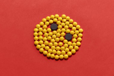 Çember şeklinde yatan sarı ve siyah haplar, kırmızı arka planda izole edilmiş bir yüz. Sağlık ve tedavi kavramı.