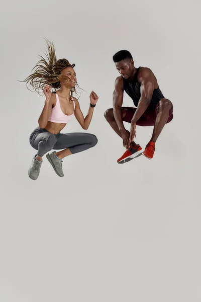 Πιο ψηλά. Full length shot of young muscle african american man and sportive mixed race woman jumping, γιορτάζοντας το μεγάλο επίτευγμα, χαρά απομονωμένη πάνω από γκρι φόντο — Φωτογραφία Αρχείου