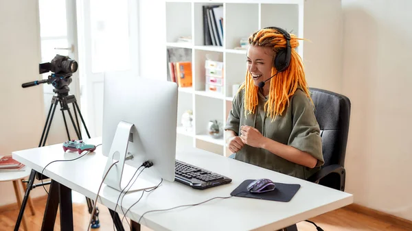 Kul. Kvinnlig eportspelare, kvinna i hörlurar gör ansikten, spela online videospel på PC medan du spelar in, filma vlog i dagtid — Stockfoto