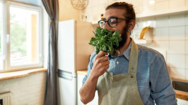 Genç adama yaklaş, önlüklü İtalyan aşçı fesleğen yaprağı koklarken mutfakta hazır bekliyor. Ev konseptinde aşçılık