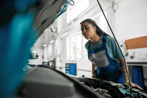 Autocuidado. Mujer afroamericana joven, mecánico profesional abriendo la capucha del coche y chequeando el coche en el taller de reparación de automóviles — Foto de Stock
