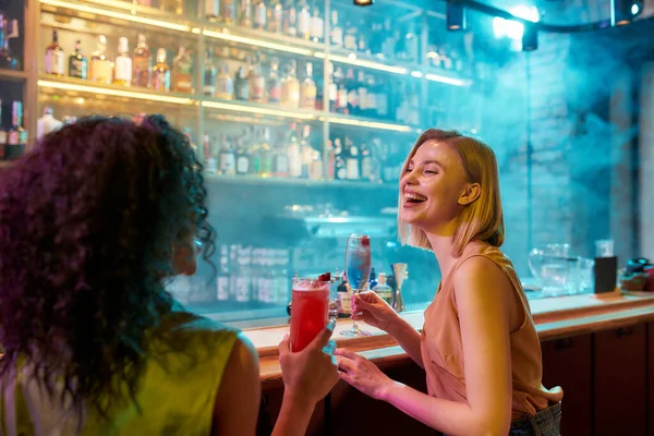 Momentos de felicidad. Dos mujeres divirtiéndose, bebiendo cócteles mientras están sentadas en el mostrador del bar. Amigos pasando tiempo en el club nocturno, restaurante — Foto de Stock