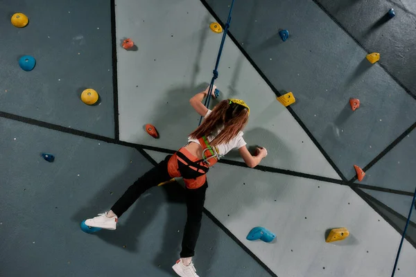 Para cima. Menina vestindo equipamentos de segurança e treinamento arnês na parede de escalada artificial dentro de casa. Conceito de formação em Bouldering — Fotografia de Stock