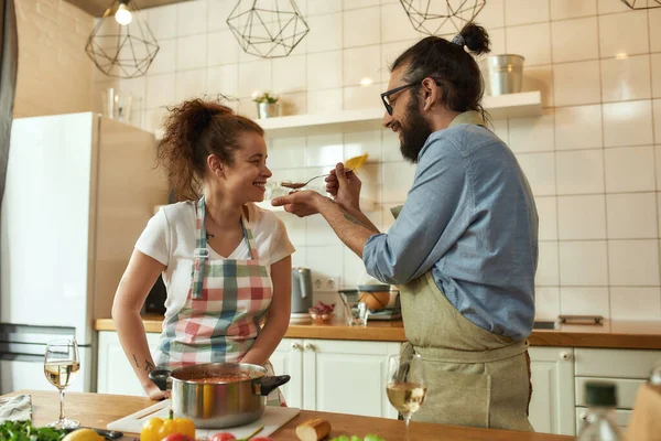 Hombre italiano, cocinero alimentando a su novia, dejándola probar la sopa. Pareja alegre preparando una comida juntos en la cocina. Cocina en casa, Cocina italiana — Foto de Stock