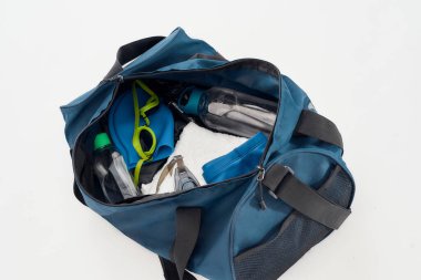 Yüzme takımları hazır. Yüzme gözlüklü, şapkalı ve şapkalı spor çantasının üst görüntüsü, gri arka planda izole edilmiş havlu ve su şişesi.