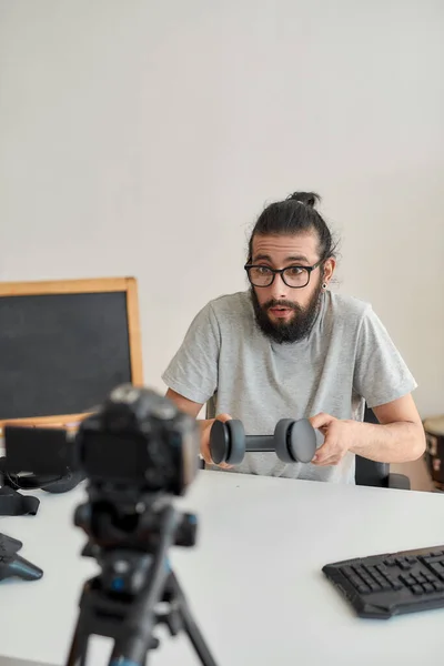 Man teknik bloggare i glasögon talar, håller hörlurar, medan du spelar in video blogg eller vlog om nya prylar hemma studio — Stockfoto