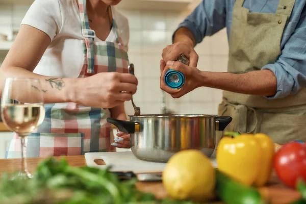 Cortado tiro de hombre añadiendo pimienta, especia a la sopa, mientras que la mujer revolviendo con una cuchara. Pareja preparando una comida juntos en la cocina. Cocina en casa, Cocina italiana — Foto de Stock