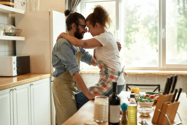 Un giovanotto che guarda la sua ragazza, che si abbraccia mentre sta in cucina. Coppia che abbraccia mentre si fa la pizza con le verdure al chiuso. Cucinare insieme, hobby, lifestyle — Foto Stock