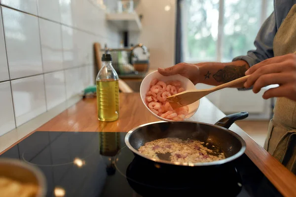 Förfölj smaken. Närbild av människan lägga till räkor till sauteed vitlök och lök i stekpannan. Koka maträtt med skaldjur. Koncept för medelhavsköket — Stockfoto