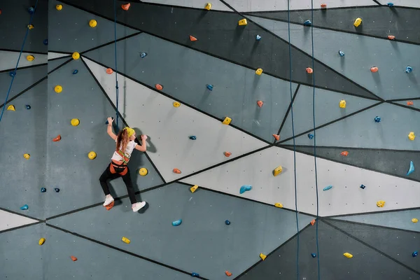 Chica en equipo de seguridad y entrenamiento de arnés en la pared de escalada artificial en el interior. Concepto de formación de Bouldering —  Fotos de Stock