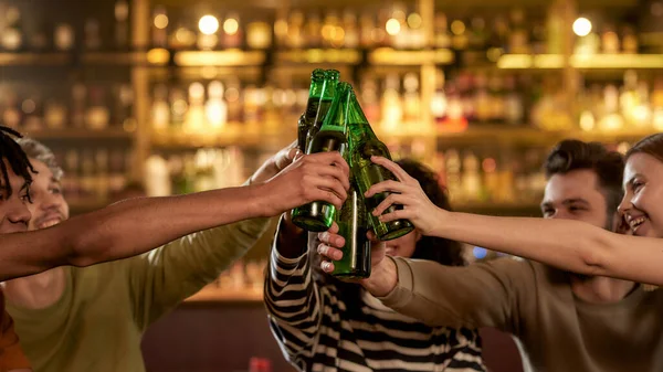Primer plano de las manos de las personas en el bar tintineo botellas mientras beben cerveza juntos. Gente, ocio, amistad y entretenimiento — Foto de Stock