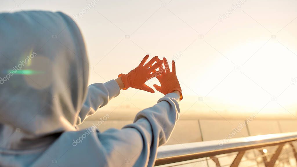 Protection against infection. Woman wearing protective gloves, reaching out her hands to the light while watching the sunrise. Coronavirus, epidemic, safety concept