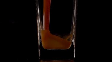 Favori Lezzet. Şeffaf bir bardağa siyah arkaplana domates suyu dökerken çekilen süper yavaş çekim. Kapatın. Sağlıklı içecek, vitamin konsepti