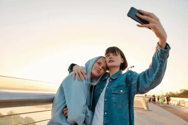 Lesbisches Paar steht auf der Brücke, posiert für ein Selfie-Foto und beobachtet gemeinsam den Sonnenaufgang — Stockfoto