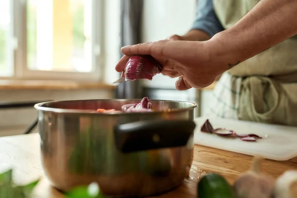 Närbild av händerna på människan, kock kock lägga lök till potten med hackade grönsaker samtidigt förbereda en måltid i köket — Stockfoto