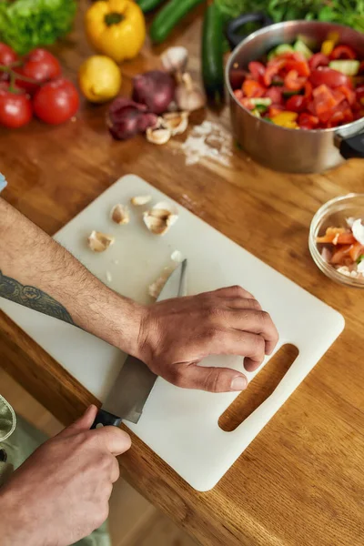 Közelkép a kezét az ember, séf szakács vágás fokhagyma a vágódeszka, miközben elkészíti az ételt a konyhában — Stock Fotó