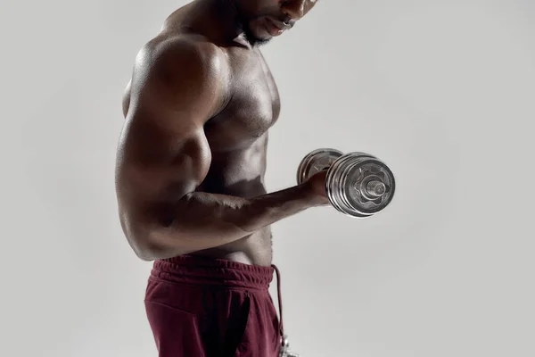 Gehakt schot van jonge gespierde Afro-Amerikaanse man die gewichten tilt, geïsoleerd boven grijze achtergrond. Sport, workout, bodybuilding concept — Stockfoto