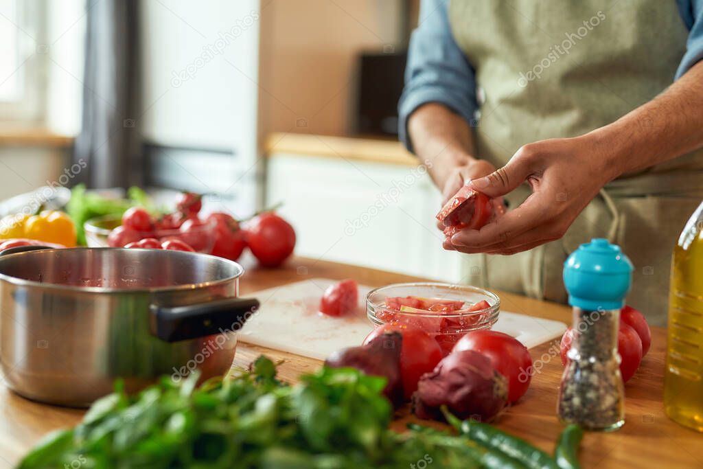 Close up of man cook holding knife, cutting tomatoes while preparing healthy meal with vegetables in the kitchen. Italian cuisine concept