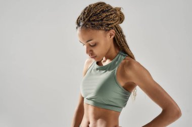 Gri arka planda yalnız poz veren spor kıyafetli güzel bir kadın portresi.