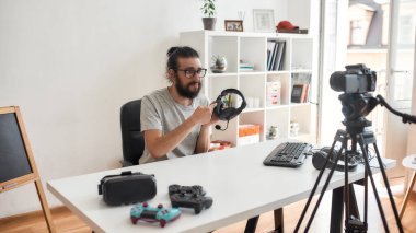 Erkek teknoloji blogcusu tutuyor, kulaklıklara işaret ediyor, video blogu ya da video blogu kaydederken hoşnutsuz görünüyor.