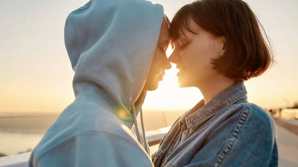 Dotyk miłości. Lesbijki ściskające się na moście, patrzące na siebie przed pocałunkiem podziwiając razem wschód słońca — Zdjęcie stockowe