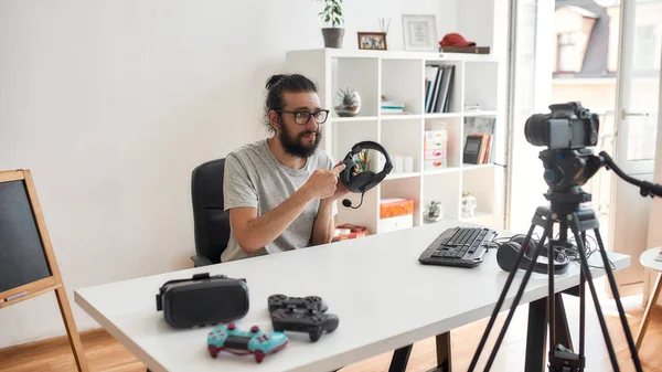 Man teknik bloggare håller, pekar på hörlurar, ser missnöjd medan du spelar in video blogg eller vlog om nya prylar hemma studio — Stockfoto