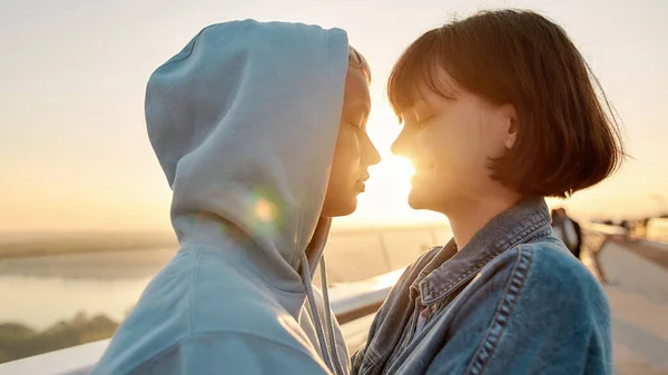 Pareja de lesbianas abrazándose en el puente, mirándose antes de besarse mientras admiran el amanecer juntos —  Fotos de Stock