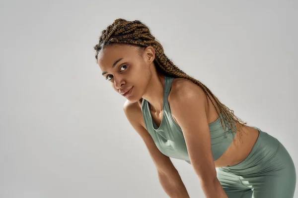 Portrait d'une femme de fitness athlétique épuisée en tenue de sport se reposant après l'entraînement, regardant la caméra tout en restant isolée sur fond gris — Photo