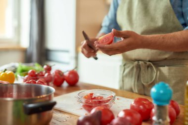 Genç bir adamın bıçakla yemek pişirirken domates keserken mutfakta sebzelerle sağlıklı bir yemek hazırlarken görüntüsü. İtalyan mutfağı kavramı