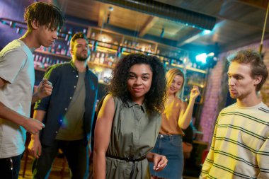 Şarkıyı hisset. Çekici melez genç kadın kameraya gülümserken eğleniyor, gece kulübünde arkadaşlarıyla dans ediyor.