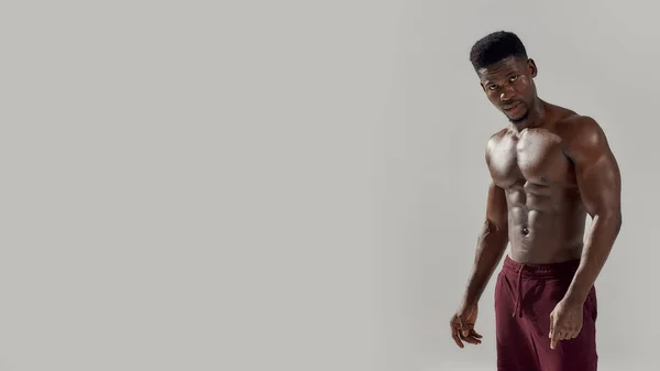 Jovem musculoso afro-americano olhando para a câmera, mostrando seu tronco nu enquanto posava sem camisa isolado sobre fundo cinza. Esportes, treino, conceito de musculação — Fotografia de Stock