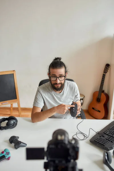 Чоловічий технологічний блогер в окулярах тримає, вказуючи на мишку під час запису відео блогу або блогу про нові гаджети вдома — стокове фото