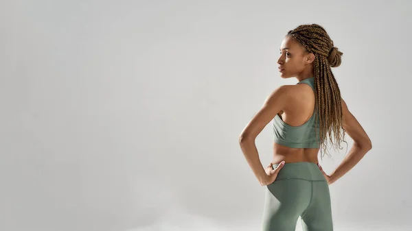 Vista posterior de la joven atlética de raza mixta fitness mujer en ropa deportiva posando en el estudio, aislado sobre fondo gris — Foto de Stock