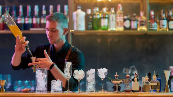 Jovem garçom masculino derramando, misturando ingredientes enquanto faz coquetel clássico bebida alcoólica no balcão do bar na boate — Fotografia de Stock