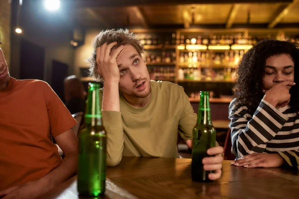 A fiatalember csalódottan néz, miközben sportmeccset néz a TV-ben, sört iszik és szurkol a csapatnak a bárban. Emberek, szabadidő és szórakozás fogalma — Stock Fotó