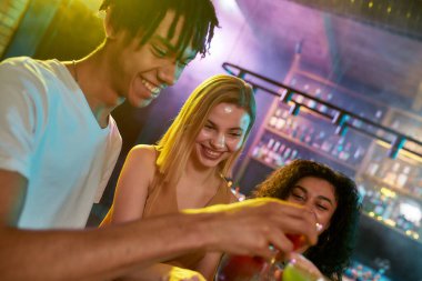 Kendini eğlenceyle doldur. Bir grup arkadaş, genç kadın ve erkek eğlenirken gülümsüyor, kokteyl içiyor, gece kulübünde vakit geçiriyor.