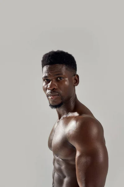 Retrato de jovem musculoso afro-americano com tronco nu olhando para a câmera enquanto posando sem camisa isolado sobre fundo cinza. Esportes, treino, conceito de musculação — Fotografia de Stock