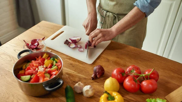 Közelkép a kezét az ember, séf szakács vágás hagyma a vágódeszka, miközben elkészíti az ételt a konyhában — Stock Fotó