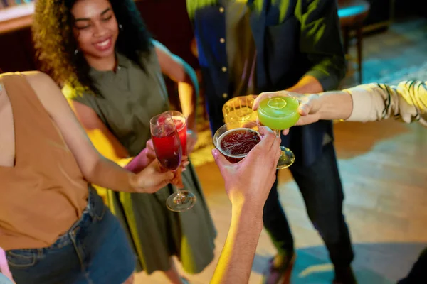 Foto recortada de grupo de amigos, adultos jóvenes, hombres y mujeres divirtiéndose, brindando, bebiendo cócteles de pie en un club nocturno — Foto de Stock