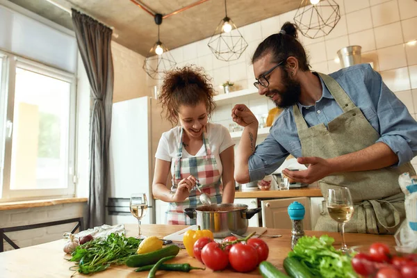 Hombre italiano añadiendo pimienta, especias a la sopa mientras la mujer revolviendo y sonriendo, pareja preparando una comida juntos en la cocina — Foto de Stock