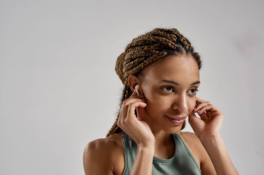 Müzikle çalışmak. Kablosuz kulaklık takan ve gri arka planda tek başına dikilmiş gülümseyen mutlu, melez kadın portresi.