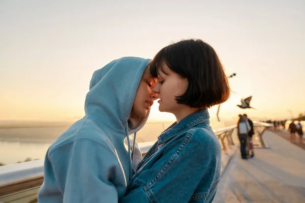 Lesbisches Paar umarmt sich auf der Brücke, küsst sich und bewundert gemeinsam den Sonnenaufgang — Stockfoto