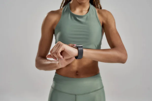 Primer plano de una atlética mujer de raza mixta montando su smartwatch o comprobando los resultados de fitness mientras está aislada sobre un fondo gris — Foto de Stock