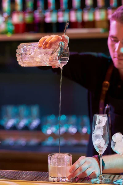 Jovem garçom masculino derramando, misturando ingredientes enquanto faz coquetel clássico bebida alcoólica no balcão do bar na boate — Fotografia de Stock