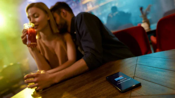 Mesaj de la soţie. Bărbatul necredincios petrece timp cu o altă femeie flirtând în bar, bucurându-se de băuturi și conversații. Inselat, concept de infidelitate — Fotografie, imagine de stoc